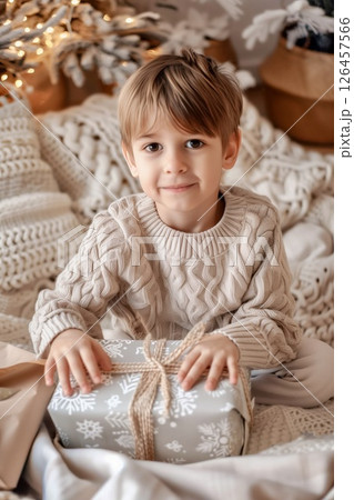 A young boy in a cozy sweater excitedly unwraps a gift during a festive holiday gathering at home surrounded by decorations 126457566