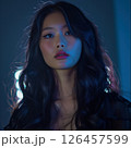 Young woman with wavy hair poses confidently in soft blue light, showcasing a modern aesthetic in a creative studio setting 126457599
