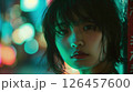 A young woman gazes thoughtfully at the camera under colorful neon lights in a bustling urban setting at night 126457600