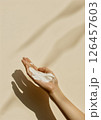 A hand holding a creamy skincare product against a soft beige background with gentle shadows in natural light 126457603