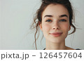 A young woman smiling gently with soft features and loose hair against a light background in a serene indoor setting 126457604