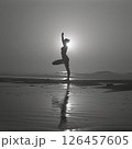 A silhouetted figure practices yoga on a serene beach at sunset, creating a peaceful atmosphere with reflections on the water 126457605