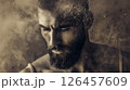 A focused man with a beard surrounded by swirling dust in a dramatic studio setting during a creative photo shoot 126457609