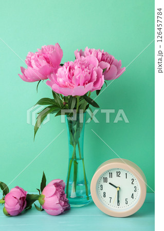 Romantic background with alarm clock and pink peonies on mint background. Vertical photo 126457784