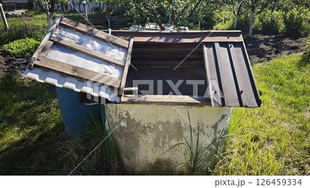 Old concrete well with a wooden lid standing on green grass in a sunny countryside garden. Concept of traditional water source and rural sustainability 126459334