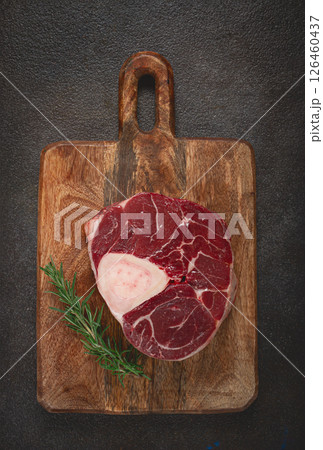 a shank on the bone, raw meat for ossobuco, on a wooden chopping board, with a branch of rosemary, top view, no people. 126460437