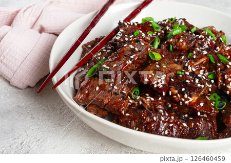 Crispy beef, with green onions and sesame seeds, in a bowl with chopsticks, on a textured surface, on a light background, no people Crispy beef, with green onions and sesame seeds, in a bowl with chopsticks, on a textured surface, on a light background, no people 126460459