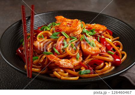udon stir-fry shrimp noodles with red bell pepper and green onion, served in a black bowl, with chopsticks, dark background, udon stir-fry shrimp noodles with red bell pepper and green onion, served in a black bowl, with chopsticks, dark background, 126460467