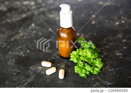 Brown glass bottle with essential oil or creme, vitaminen and healing green plant on the dark rough texture background. 126460580