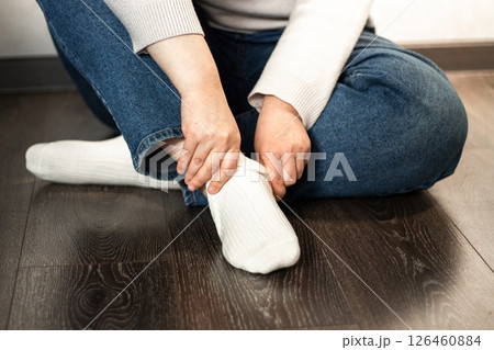 Girl pulling up cozy white socks, bare legs visible. Great for hosiery promotions, self-care visuals, or minimalist fashion concepts. 126460884