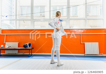 Female fencer putting on protective gear before match indoors. Female fencer putting on protective gear before match indoors. 126460905