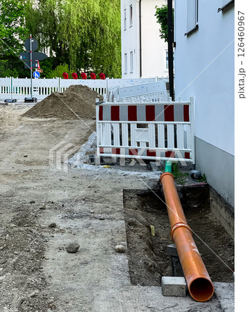 Construction site with an orange drainage pipe, white barriers, and a pile of dirt.  126460967