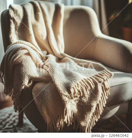 A cozy throw blanket mockup draped over the arm of a chair, with a soft-focus background in muted colors, creating a relaxing and welcoming ambiance for a peaceful space. 126461042