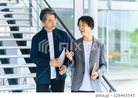 オフィスの通路でノートパソコンを持って立つ2人のビジネスパーソン オフィスの通路でノートパソコンを持って立つ2人のビジネスパーソン 126463543