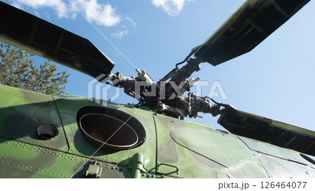 A vintage Soviet helicopter is seen from below, highlighting its rotor blades against a clear blue sky and green trees, showcasing its military design. A vintage Soviet helicopter is seen from below, highlighting its rotor blades against a clear blue sky and green trees, showcasing its military design. 126464077