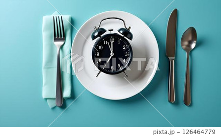 An alarm clock on a plate beside a fork and knife, symbolizing meal timing in a weight loss and health context 126464779