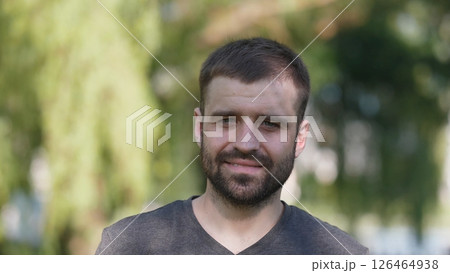 A man with a beard stands outdoors, smiling warmly. Sunlight filters through trees, creating a serene ambiance, perfect for casual socializing or portrait sessions. A man with a beard stands outdoors, smiling warmly. Sunlight filters through trees, creating a serene ambiance, perfect for casual socializing or portrait sessions. 126464938