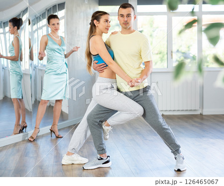 Couple in comfortable sports clothes learns tango dancing during individual lesson Couple in comfortable sports clothes learns tango dancing during individual lesson 126465067