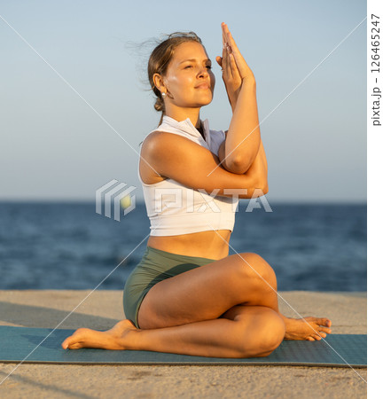 Sportive girl practicing eagle pose of yoga on seashore Sportive girl practicing eagle pose of yoga on seashore 126465247