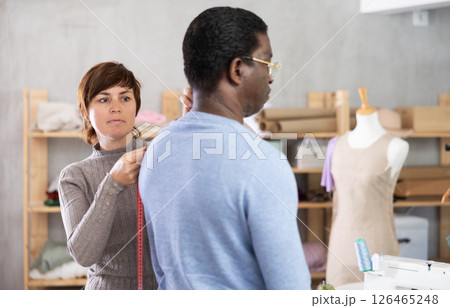 Woman tailor takes measurements from African American man client Woman tailor takes measurements from African American man client 126465248