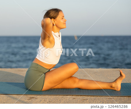 Young woman practicing vinyasa yoga asanas on mat on seashore Young woman practicing vinyasa yoga asanas on mat on seashore 126465286