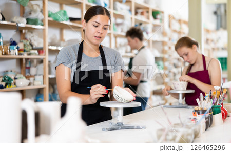 Young woman painting ceramic cup in ceramic workshop 126465296