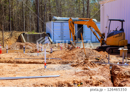 Excavator digs at construction site surrounded by trench, preparing foundation, to utility installations. 126465350