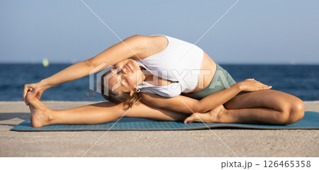On windy day young slender woman does yoga near sea doing Parivritta Janu Shirshasana On windy day young slender woman does yoga near sea doing Parivritta Janu Shirshasana 126465358