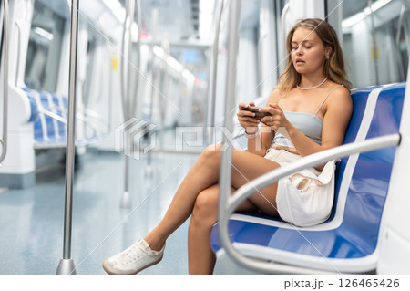 Young woman sitting in subway car with phone Young woman sitting in subway car with phone 126465426