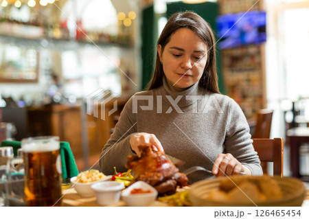 Positive brunette having lunch in cafe with roasted ham hock and beer Positive brunette having lunch in cafe with roasted ham hock and beer 126465454