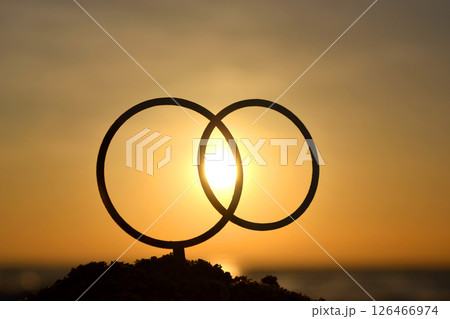 Black outlines of wedding rings at dawn and sunset on yellow sky. Stick contours in shape of wedding rings in sand on backdrop of setting and rising sun. Concept wedding love romantic Valentine's Day 126466974