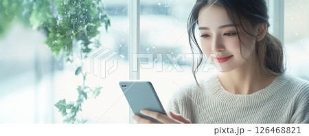 A woman enjoys her phone while sitting by the window in a cozy atmosphere. A woman enjoys her phone while sitting by the window in a cozy atmosphere. 126468821