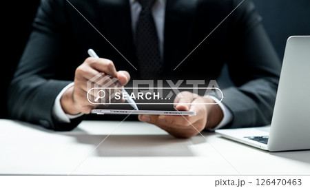 Businessman using a tablet and showing a search engine bar icon on the screen. Laptop on the desk. Technology innovation on the virtual screen. Concept of technology and web network Businessman using a tablet and showing a search engine bar icon on the screen. Laptop on the desk. Technology innovation on the virtual screen. Concept of technology and web network 126470463