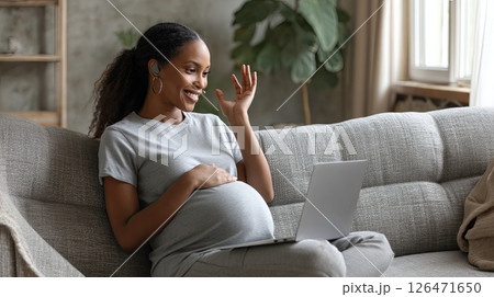 Young pregnant African American woman in front of laptop monitor at home. The young woman smiles brightly during her online consultation, embracing her pregnancy with excitement. 126471650