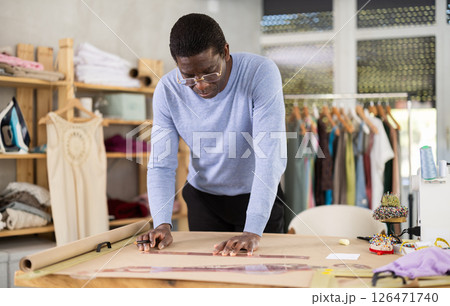 Male tailor draws sketch of future clothing on paper using patterns in sewing workshop Male tailor draws sketch of future clothing on paper using patterns in sewing workshop 126471740