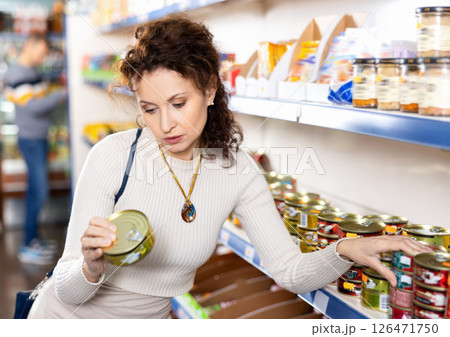 In Russian goods store, woman choose canned sprats in oil 126471750
