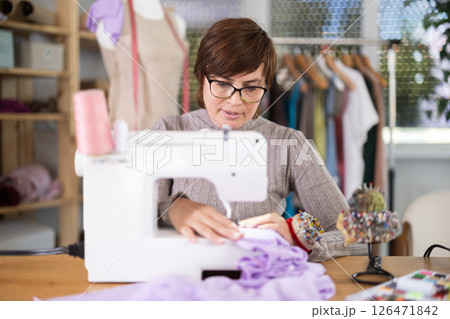 Female clothing designer stitching fabric on sewing machine in studio Female clothing designer stitching fabric on sewing machine in studio 126471842