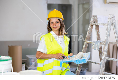 Portrait of woman painter in a protective helmet and vest with paint roller Portrait of woman painter in a protective helmet and vest with paint roller 126471875