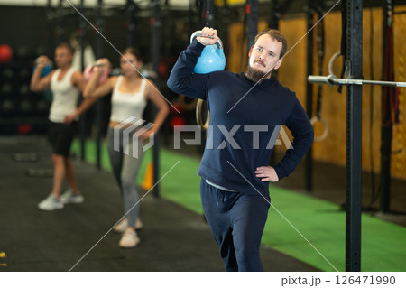 Bearded man doing kettlebell overhead shoulder press in gym 126471990
