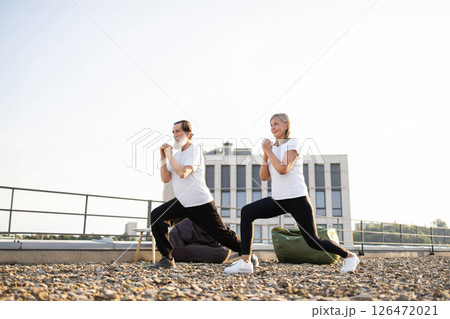 Elderly man and woman performing yoga stretches outdoors promoting health, fitness, and active lifestyle benefits. Energizing activity embracing physical and mental well-being. 126472021
