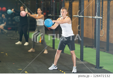 Sporty young man exercising with kettlebell in gym at group workout Sporty young man exercising with kettlebell in gym at group workout 126472132