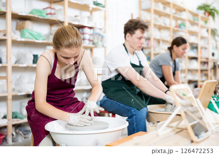 Young girl creates clay product on potter wheel in workshop 126472253