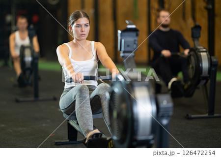 Girl exercising on rowing machine during intense full body workout 126472254