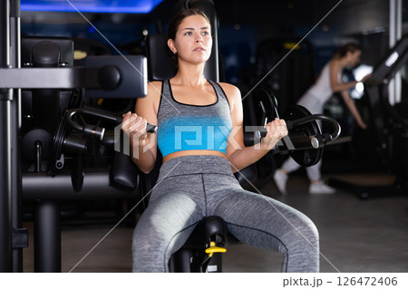 Sportive young girl training on arm curl machine in gym Sportive young girl training on arm curl machine in gym 126472406