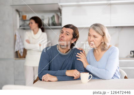 Senior woman sits near adult son and comforts him during quarrel with wife. 126472446