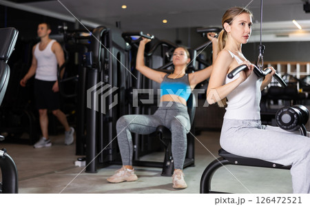 Sportive young girl training on lat pull down machine in gym Sportive young girl training on lat pull down machine in gym 126472521