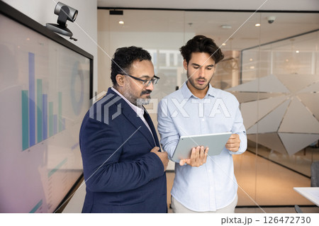 Two focused businessmen analyzing performance metrics displayed on tablet Two focused businessmen analyzing performance metrics displayed on tablet 126472730