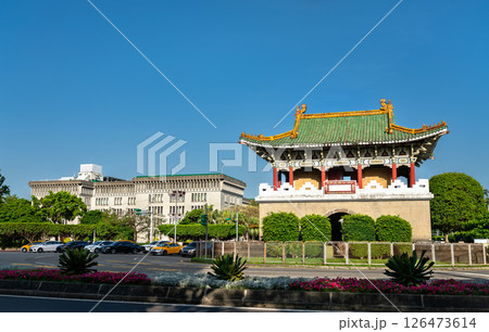 East Gate, a traditional Chinese-style gate tower with green tiles and ornate architecture stands at a roundabout in central Taipei, Taiwan, surrounded by palm trees and urban buildings under a clear 126473614