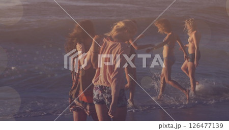 Group of friends walking on beach over bokeh lights image Group of friends walking on beach over bokeh lights image 126477139