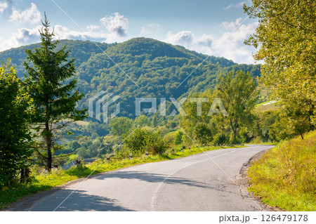 mountain pass on a sunny evening. road winding down the hill. trees on the roadside. forested hill in the distance 126479178